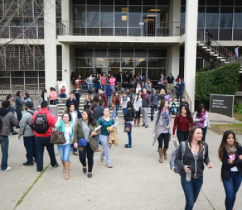A crowd of students walking by the main entrance of Bizzini Hall. 
