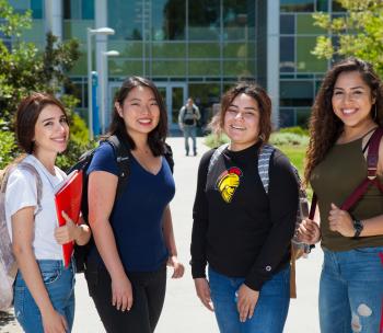 Four students on campus smiling at the camera.