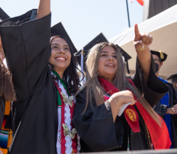Two graduates look out to the crowd at a Stan State Commencement ceremony