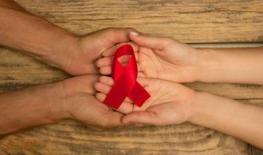 Female and male hands holding red HIV AIDS awareness ribbon.