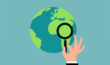 a hand holds a magnifying glass up to a globe