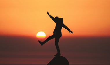 individual's silhouette balancing on a rock during sunset