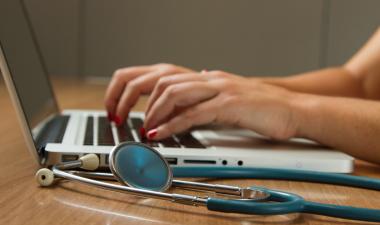 Person typing on a laptop next to a stethoscope