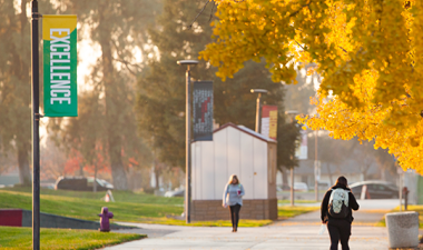 Student walking outside among fall color trees.
