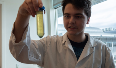 Eli Frazer holds a glass tube while standing in a science lab.