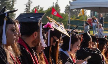 Graduates wearing their cap and gown seated. 