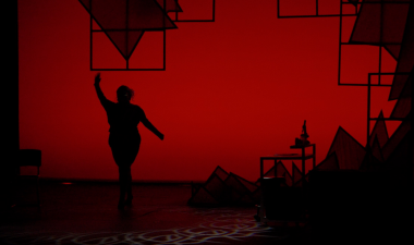 Silhouette of a performer on stage with a red background behind her.