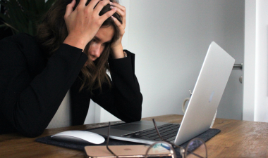 woman in long balck sleeve appearing stressed while staring at a laptop.