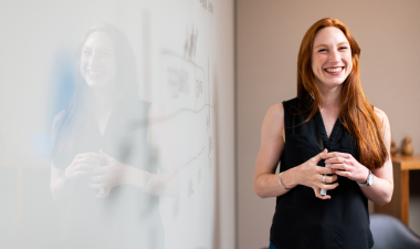 a woman smiling standing beside a whiteboard