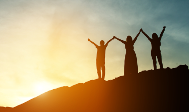 Three people holding hands on a hill, with the sun in the background