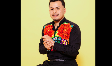 Poet yosimar reyes sitting on a stan stool. Hands together. smilling.