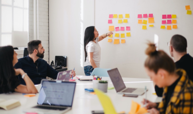 5 individuals grouped around a table reviewing notes on a board.