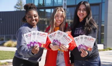 3 women standing together holding pamphlets toward the camera