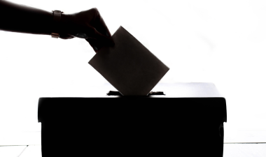 a hand placing a ballot in a box.