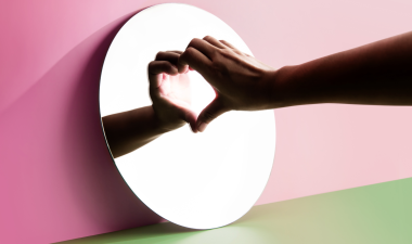 a person with one hand to a mirror, creating a heart with the reflection.
