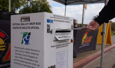 A voter slips a ballot into an official ballot box at Stanislaus State.