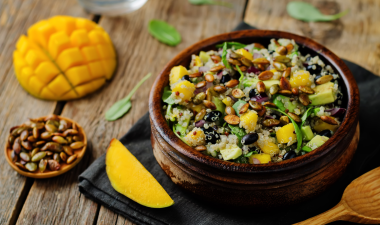 a bowl of mango and black bean salad with a cut mango on the table next to the bowl