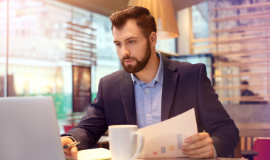 a man sitting in front of a laptop while reviewing paperwork