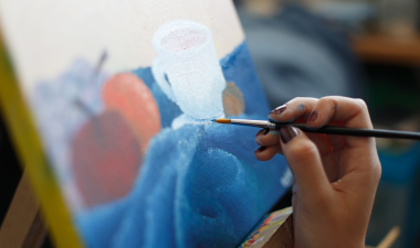 an artist painting an image of cups and fruit.