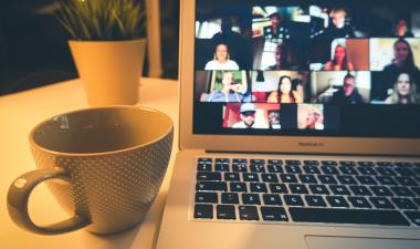 a virtual meeting taking place on a laptop screen with a cup of coffee next to the laptop