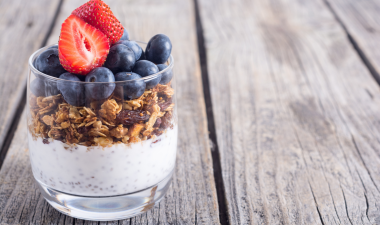 a yogurt parfait with berries in a clear glass sitting on a picnic table