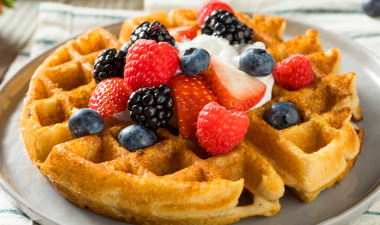 a waffle with fresh strawberries, blackberries and blueberries on top.