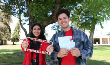 Two students holding alumni license plates and decals.