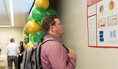 A student reads a research poster at Stan State's 2024 Research, Scholarship and Creative Activity Celebration.