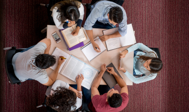 students gathered around a table studying, with books and paperwork laid across the table