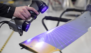 A person operates a 3D scanner, in a workshop setting.