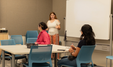 Students seated inside a classroom while an instructor speaks. 