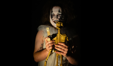 Someone with black and white clown makeup holds and plays with a skeleton toy