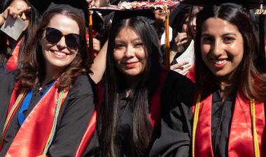 Three smiling students in regalia at Commencement ceremony.