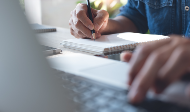 Person taking notes and looking at computer