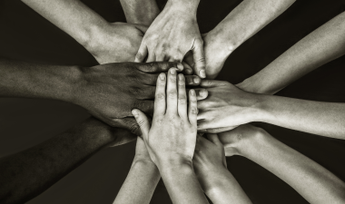 group of people from different ethnic backgrounds place hands in center.