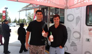 Two students holding frozen yogurt cups in front of the Yogurt Mill truck at Stan State