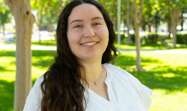 A woman in a white blouse and striped pants joyfully walks through a sunlit park, surrounded by trees and lush grass, exuding happiness and serenity.