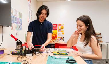 Two Stanislaus State students work together with electronic components and tools at a table in a campus lab.