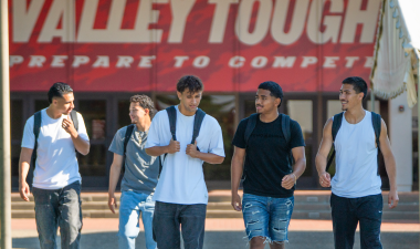 Five Stanislaus State students walk together on campus in front of the Fitzpatrick Arena.