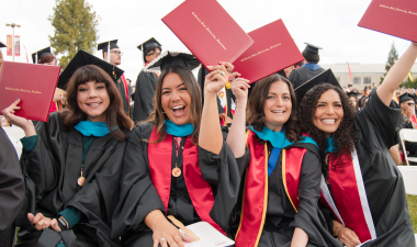 Four women graduates holding up diplomas