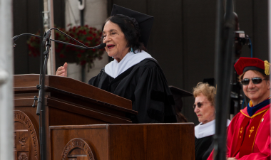 Delores Huerta stands at a lectern and speaks into a microphone.