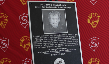 A commemorative plaque honoring James Youngblom, featuring his portrait and dedication to students, teaching and scientific research, stands on an easel against a red Stanislaus State backdrop.