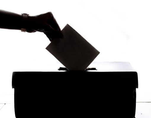a hand placing a ballot in a box.