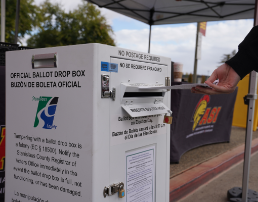 A voter slips a ballot into an official ballot box at Stanislaus State.