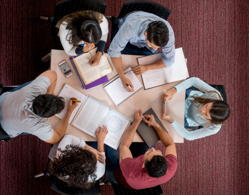 students gathered around a table studying, with books and paperwork laid across the table