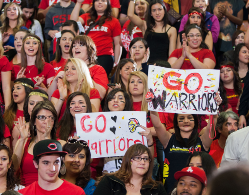 A crowd of students cheers from the bleachers at Stan State homecoming basketball game.