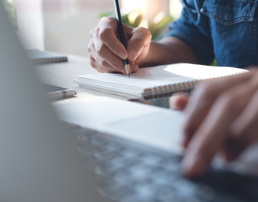 Person taking notes and looking at computer