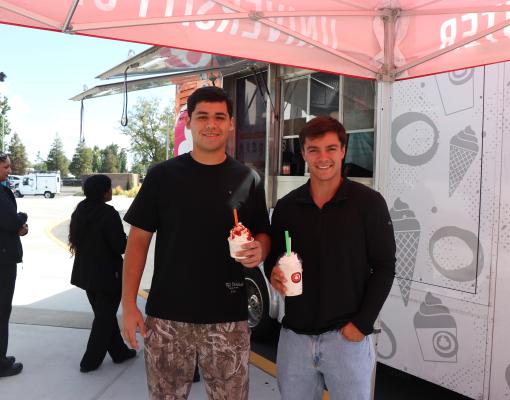 Two students holding frozen yogurt cups in front of the Yogurt Mill truck at Stan State