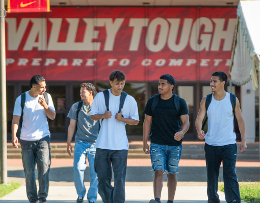 Five Stanislaus State students walk together on campus in front of the Fitzpatrick Arena.