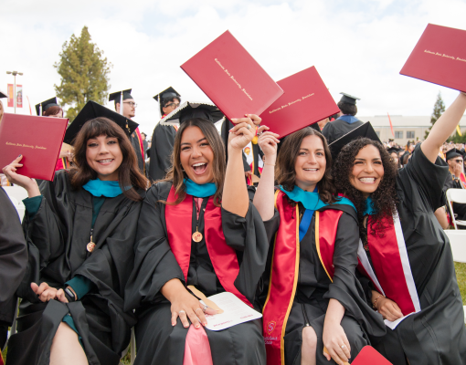 Four women graduates holding up diplomas